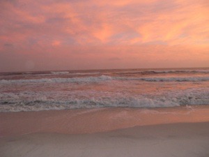 Orange and blue sunset reflecting on the ocean in the Gulf of Mexico as gentle waves cover the white sand beach.