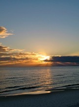 Golden sunset reflecting on calm Gulf of Mexico waters with low clouds in a deep blue sky.