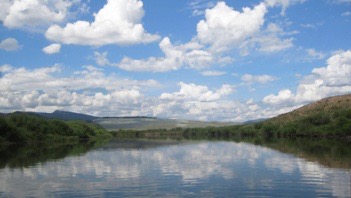 Peaceful and wide Green River flowing along summer green banks and reflecting cotton white clouds and cerulean blue Wyoming skies